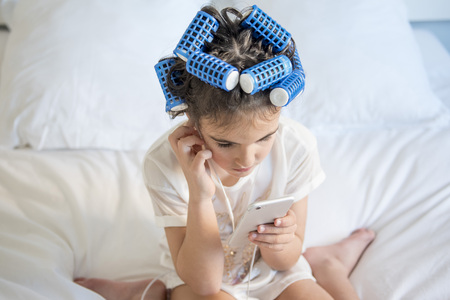little girl posing with curlers and Smartphone, surprised and happyの写真素材