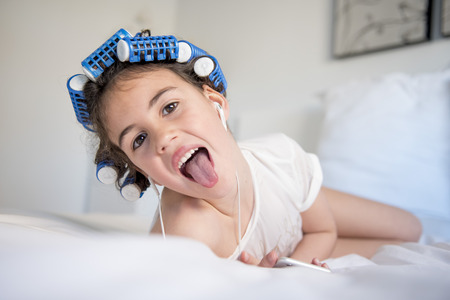 little girl posing with curlers and Smartphone, surprised and happyの写真素材