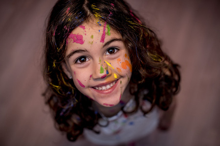 Girl smeared with paint, painting her face with a brush