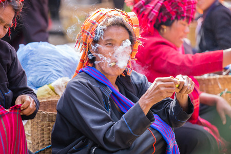 INLE LAKE, MYANMAR - December 01, 2014: an unidentified woman with cigar in traditional dress sells vegetables at market of Inn Dain Khone Village, on Inle Lake.のeditorial素材