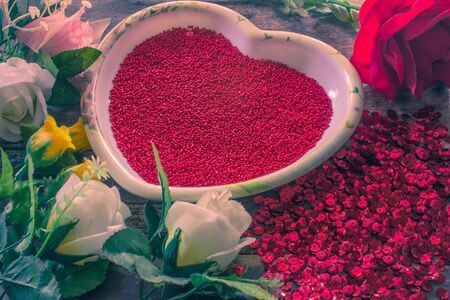 Red crystal beads in heart-shaped plate with flowers on a wooden.Valentine day background .の写真素材