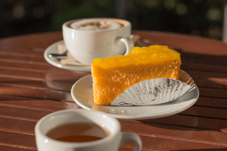 White choc macchiato coffee in white cup with tea and orange cake on wooden table.の写真素材