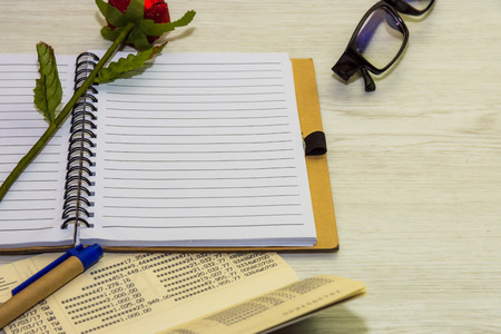 Top view of book and pen with glasses on white wooden background.
