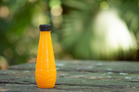 Fresh orange juice in bottles on table with green nature background.