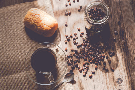 Hot coffee in a clear coffee cup and coffee beans on old wooden in a warm light on top view.の写真素材