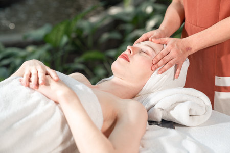 Beautiful young woman receiving head massage relaxing in spa salon, Close-up young women enjoying massage, Outdoor spa in gardens and natural light.の写真素材