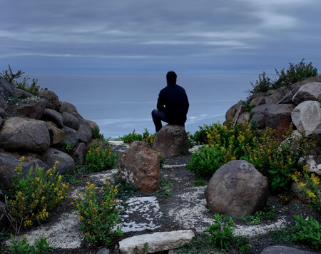 Man sitting on the edge of a cliff and looking at the seaの写真素材