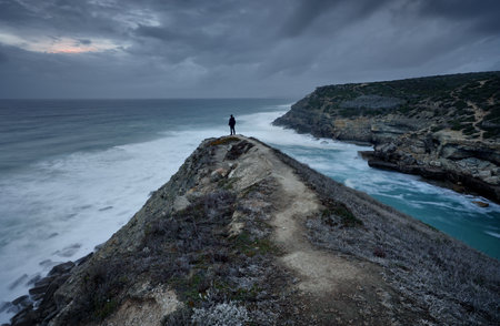 Man standing on cliff and looking at the sea in stormy weatherの写真素材