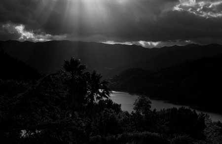 Black and white image of the sun setting over the mountains and the river.の写真素材