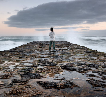 Man standing on a wooden breakwater and looking at the sea.の写真素材