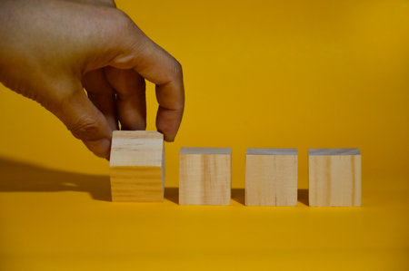 Male hand moving a square wooden block, yellow background.
