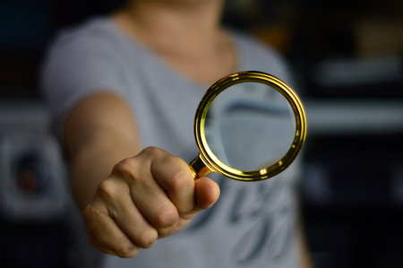 Woman holding a magnifying glass dark backgroundの写真素材