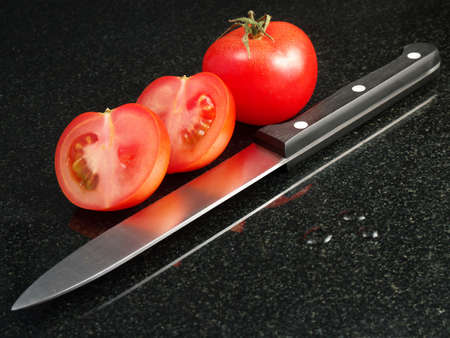 Tomatoes with vegetable knife, refelcted in black granite surface  