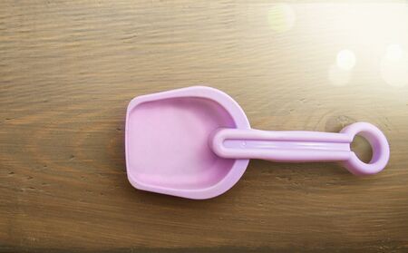 Childrens toy shovel lilac color lies on a wooden surface. Sunlight in the upper right corner.の写真素材