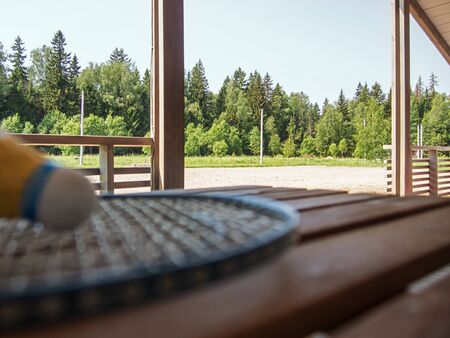 Wooden country furniture on the terrace of a country house. Blurred badminton racket and shuttlecock on wooden table. Lush green foliage in the background in focusの写真素材