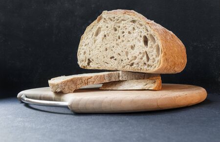 Beautiful bread made from rye and wheat flour on a wooden board on a black background. Sliced slices and half breadの写真素材