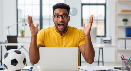 happy african american man with laptop and soccer ball at office