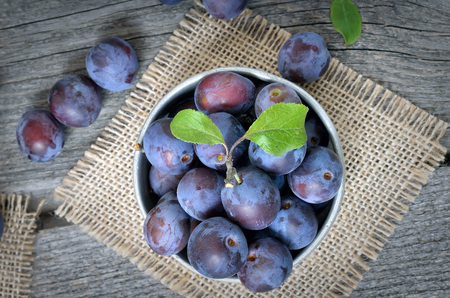 Plums in a metal bucket  a wooden background, top viewの写真素材