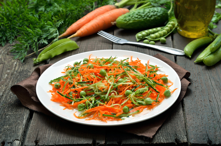 Homemade vegetable salad with carrot, cucumber, pine nuts and green peas on white plateの写真素材
