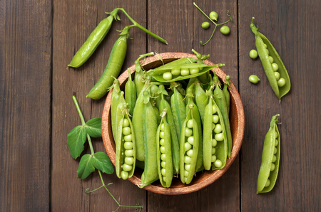 Pods of green peas in wooden bowl on a wooden background, top viewの写真素材