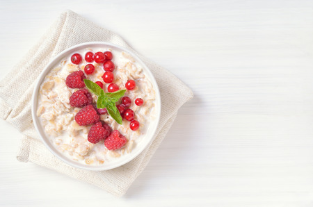 Tasty oatmeal porridge with raspberries and red currant in bowl on white table, top viewの写真素材