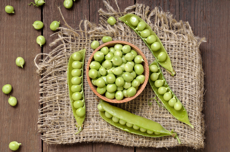 Ripe pods of green peas, fresh green peas in wooden bowl. Top view, flat layの写真素材