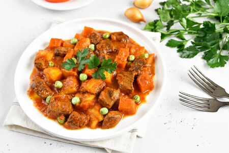 Beef stew with potatoes and carrots in tomato sauce on white plateの写真素材
