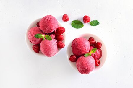 Raspberry ice cream scoop with fresh raspberries in white bowl. Cold summer dessert. Top view, flat layの写真素材