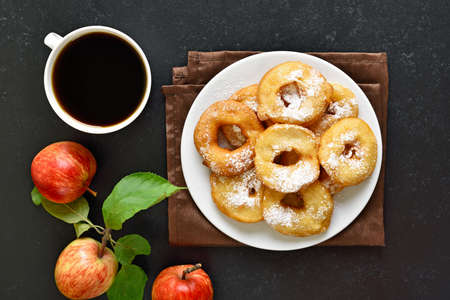 Apple rings on white plate, cup of black coffee over dark stone background. Top view, flat layの写真素材