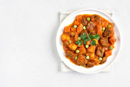 Beef stew with potatoes and carrots in tomato sauce on white plate over light background with copy space. Top view, flat layの写真素材