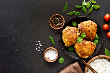 Fried chicken thighs in plate, spice and bowl of rice over dark stone background with copy space. Top view, flat layの写真素材