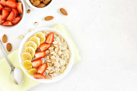 Oatmeal porridge with strawberry, banana and nuts in bowl over stone background with free text...