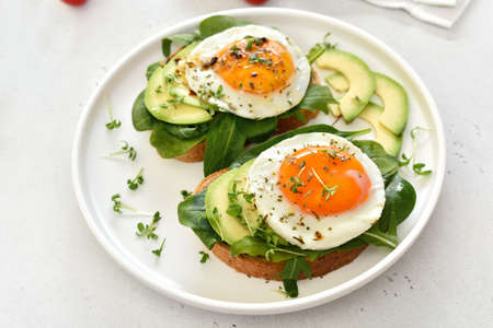 Fried eggs, avocado and greens on toasted bread. Healthy breakfast