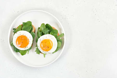 Fried eggs and greens on bread over light stone background with copy space. Top view, flat lay