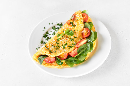 Breakfast omelette with spinach and tomato on white plate, close up viewの写真素材
