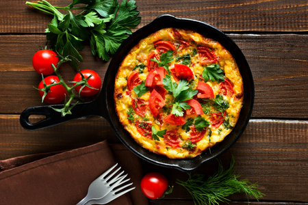 Frittata with tomatoes and spinach in frying pan over wooden background. Top view, flat layの写真素材
