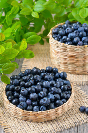 Fresh bilberry in a wicker basket on wooden table, close up viewの写真素材