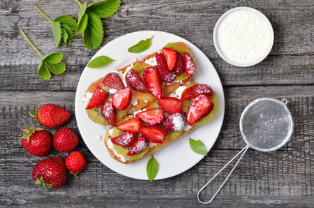 Strawberry bruschetta with kiwi and cream cheese over wooden background. Top view, flat layの写真素材