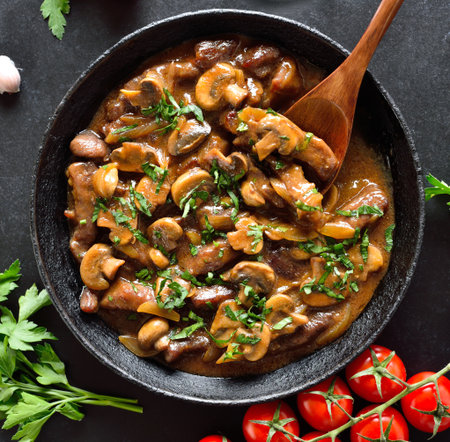 Tasty beef stroganoff with mushrooms in frying pan over black stone background. Top view, flat layの写真素材