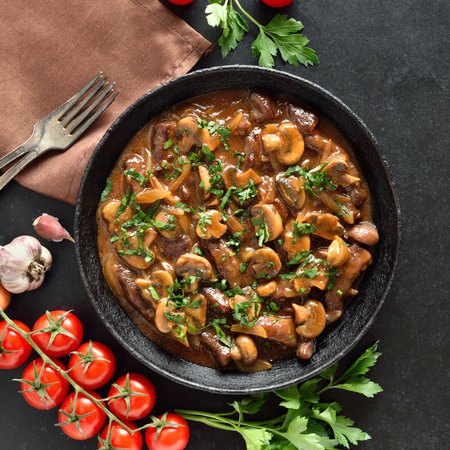 Tasty beef stroganoff with mushrooms in frying pan over black stone background. Top view, flat layの写真素材