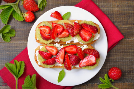 Strawberry bruschetta with kiwi and cream cheese over wooden background. Top view, flat layの写真素材