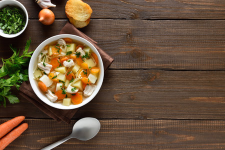Chicken noodle soup with vegetables in white bowl over wooden background with copy space. Top view, flat layの写真素材