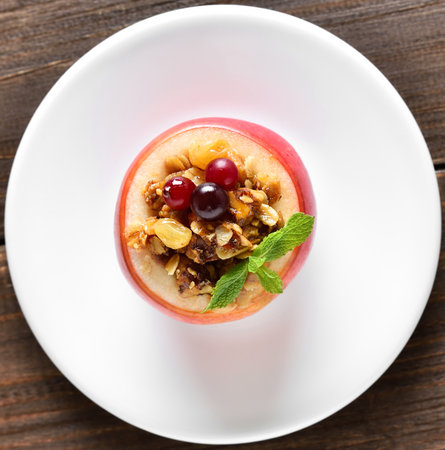 Stuffed apple with granola, cranberries, nuts and honey on plate over wooden background. Top view, flat layの写真素材