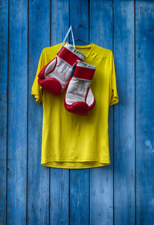 Yellow T-shirt and boxing gloves hanging on a wooden old blue wallの写真素材