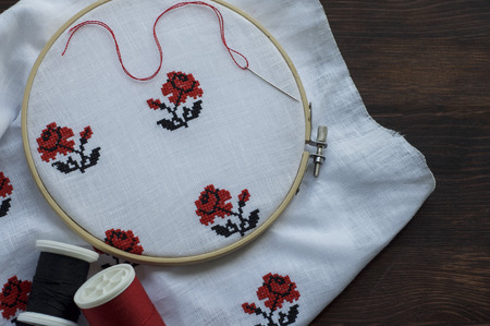 White cloth with hand-embroidered with a cross in the hoop on a wooden table, top view