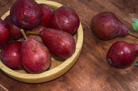 Ripe red pear in a wooden plate on the tableの写真素材