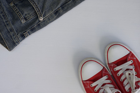 pair of red sneakers and a fragment of blue jeans on a white wooden background, top viewの写真素材