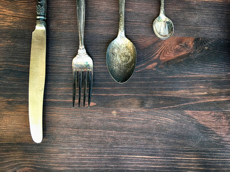 Old vintage knife, fork and spoon on a brown wooden background, top viewの写真素材