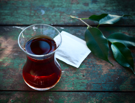 Turkish glass cup with black tea, near branch with leavesの写真素材