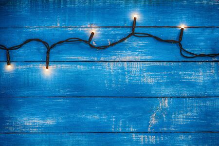 Electric garland with glowing lights on a blue wooden background, vintage toningの写真素材